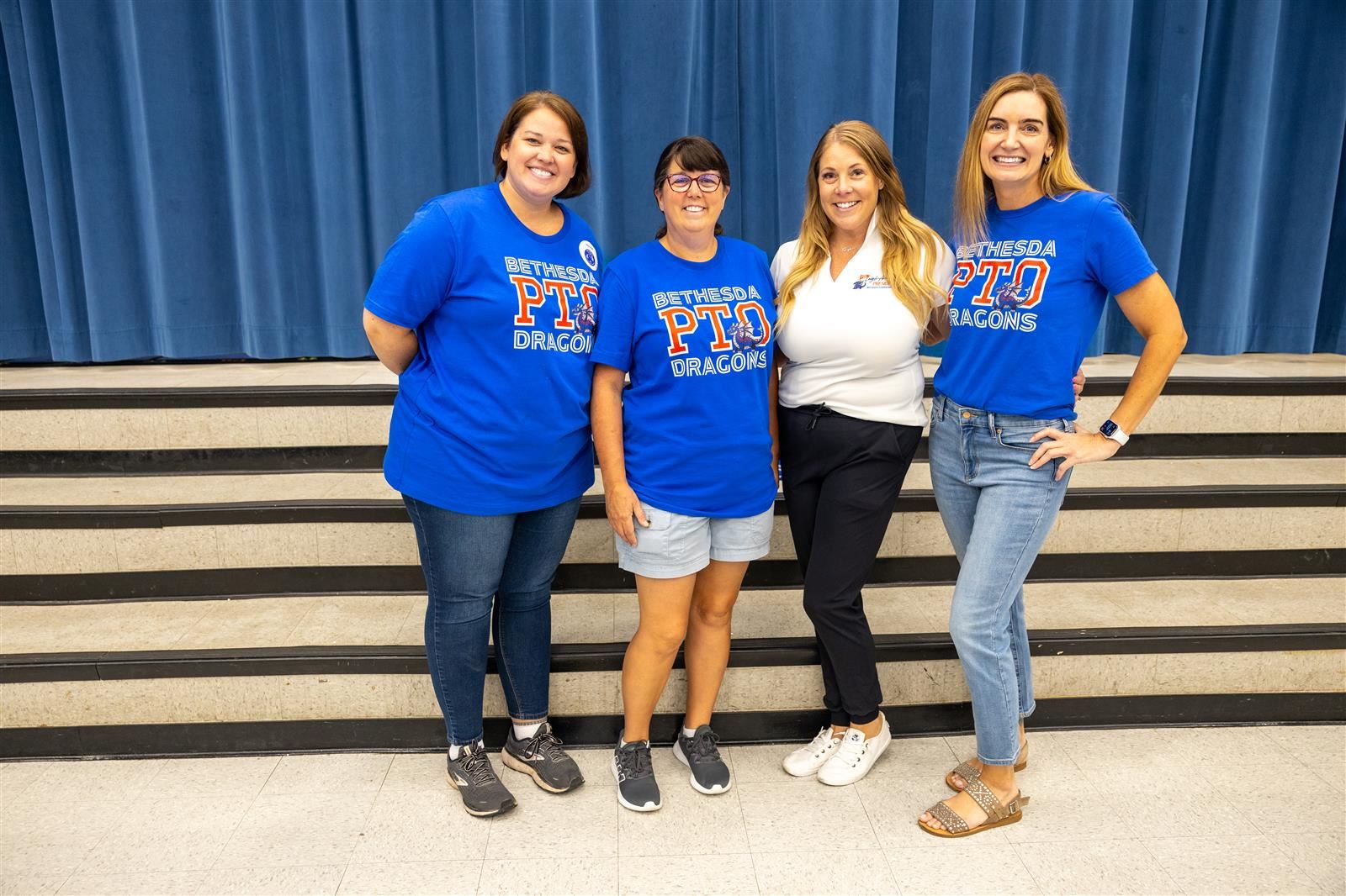 Bethesda PTO Mom's smiling in front of a blue curtain